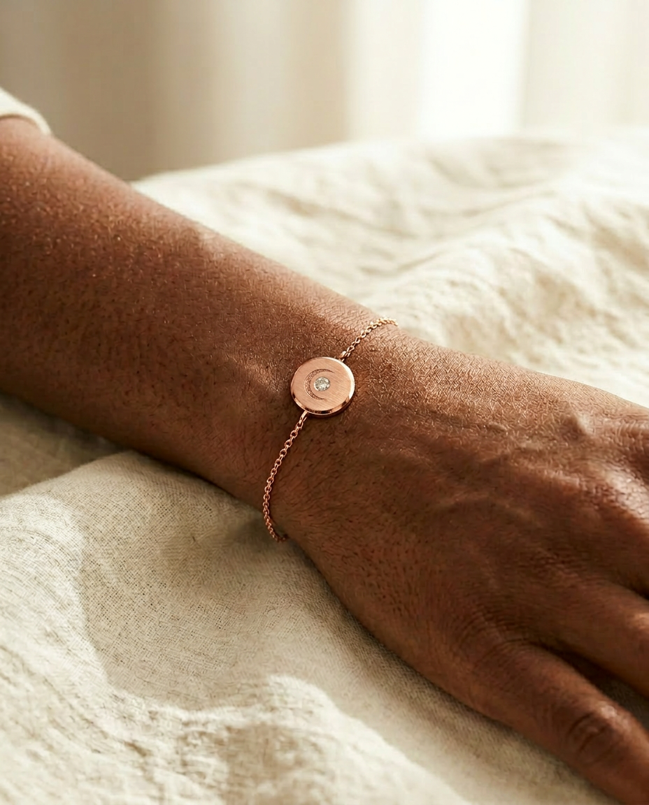 Lunar Bracelet on a Black woman's wrist resting on cream linen, fine 14K rose gold cable chain with brushed medallion charm